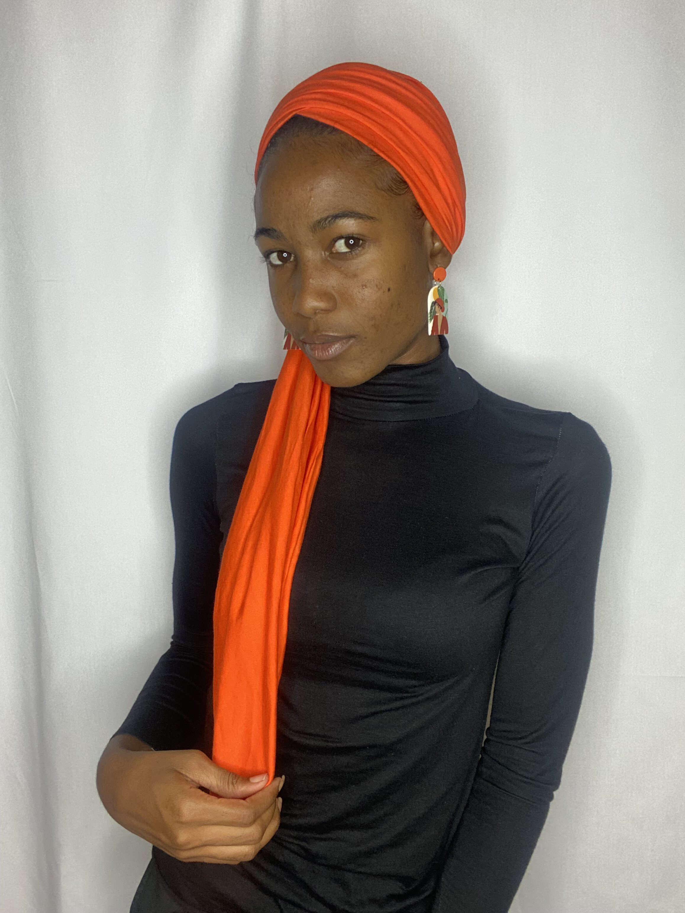 Front portrait of a woman in a coral Krown turban with statement earrings