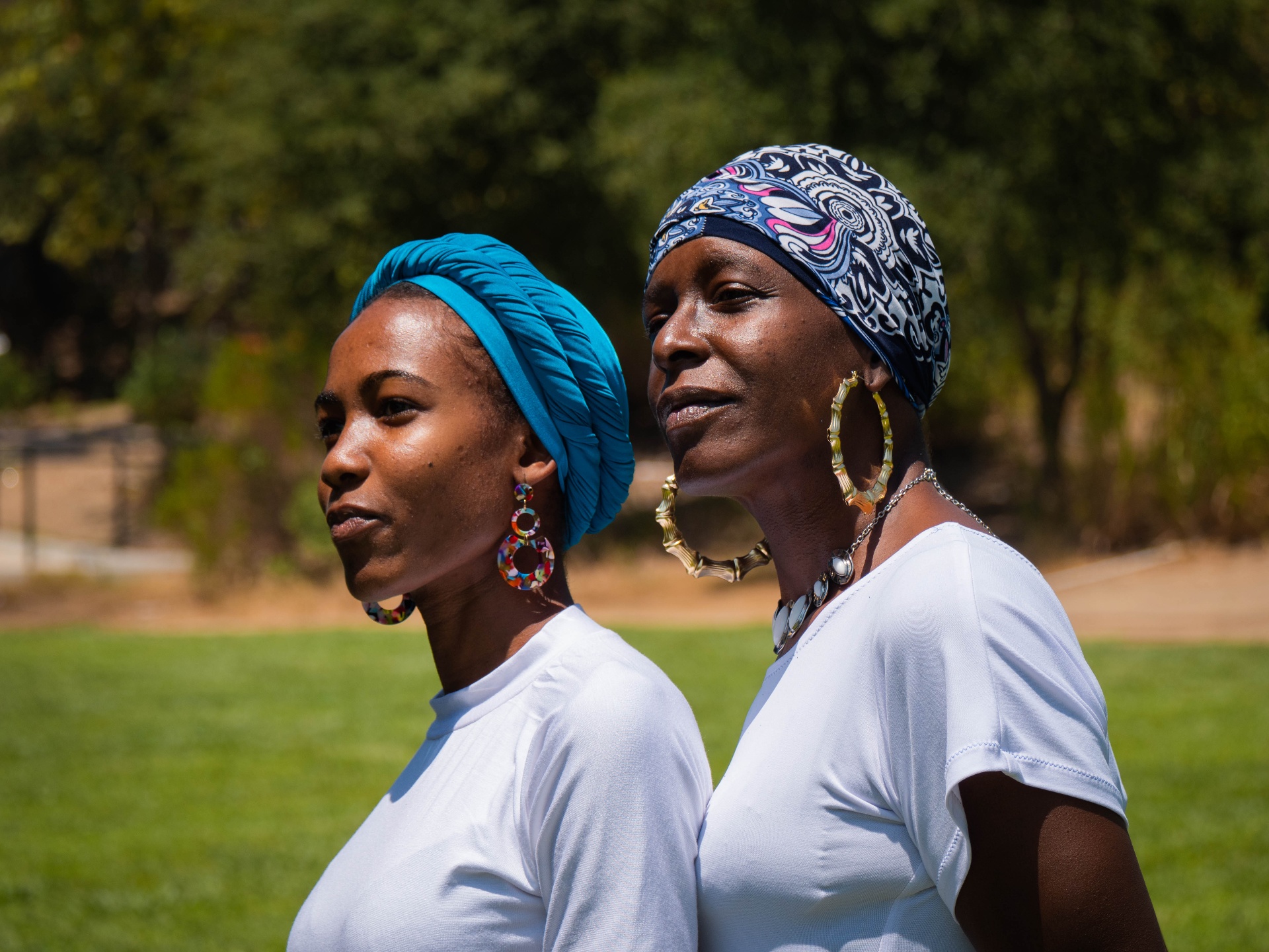 Two women outdoors modeling vibrant blue and patterned headwraps together