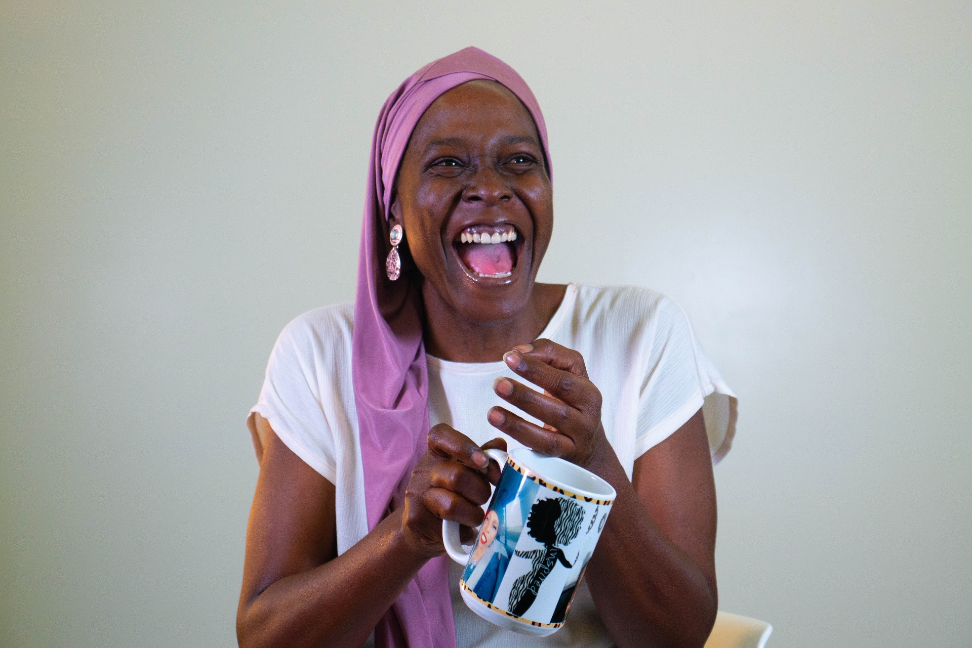 Woman laughing while wearing a soft mauve headwrap and holding a mug