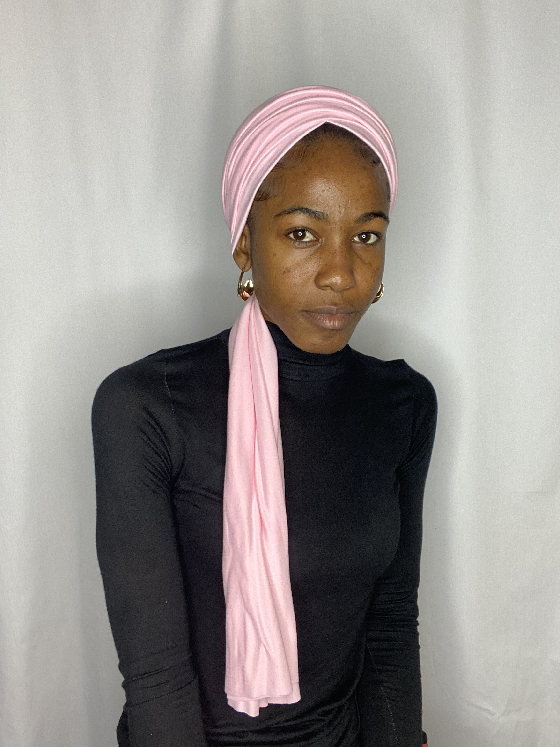 Portrait of a woman in a soft blush pink Krown styled as a headband with the tail loose down the side