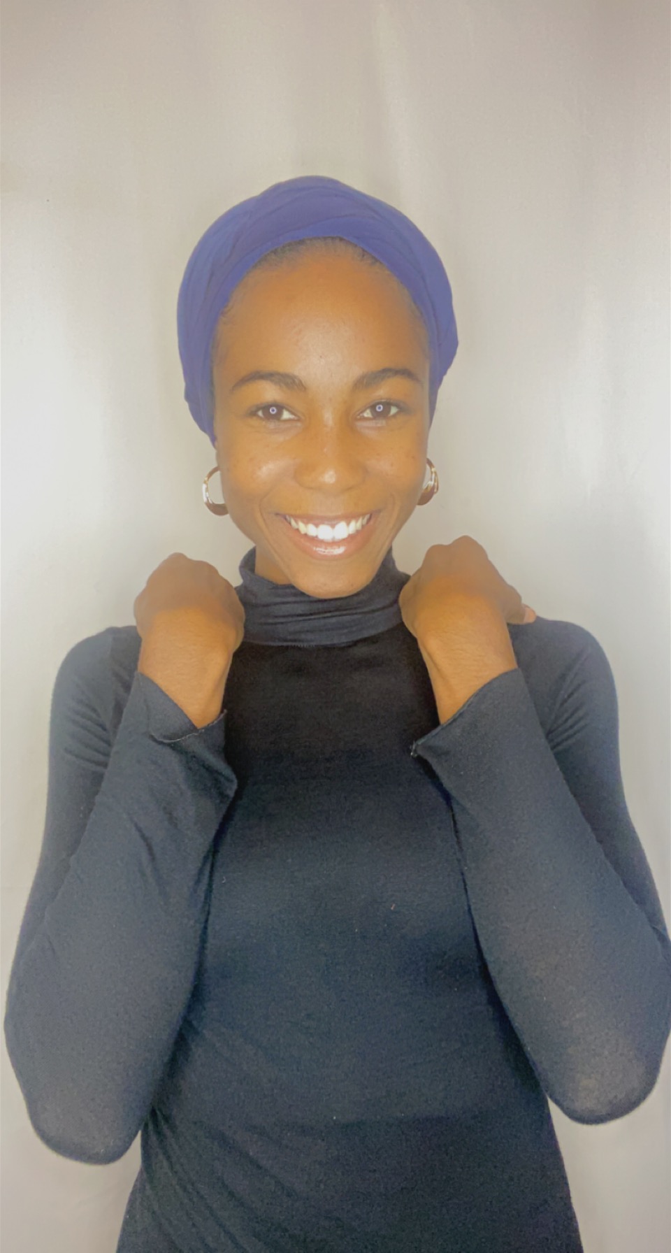 Woman laughing while wearing a deep iris Krown turban with hoop earrings