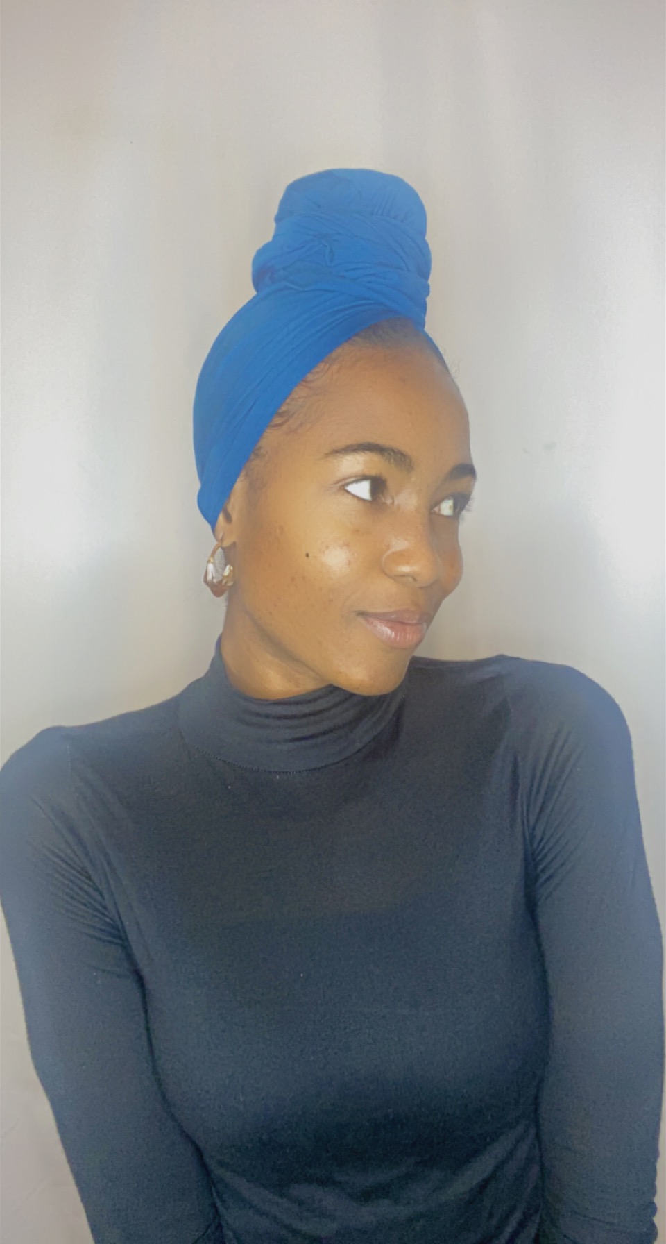 Three-quarter profile of a woman in a royal blue Krown topknot with statement earrings