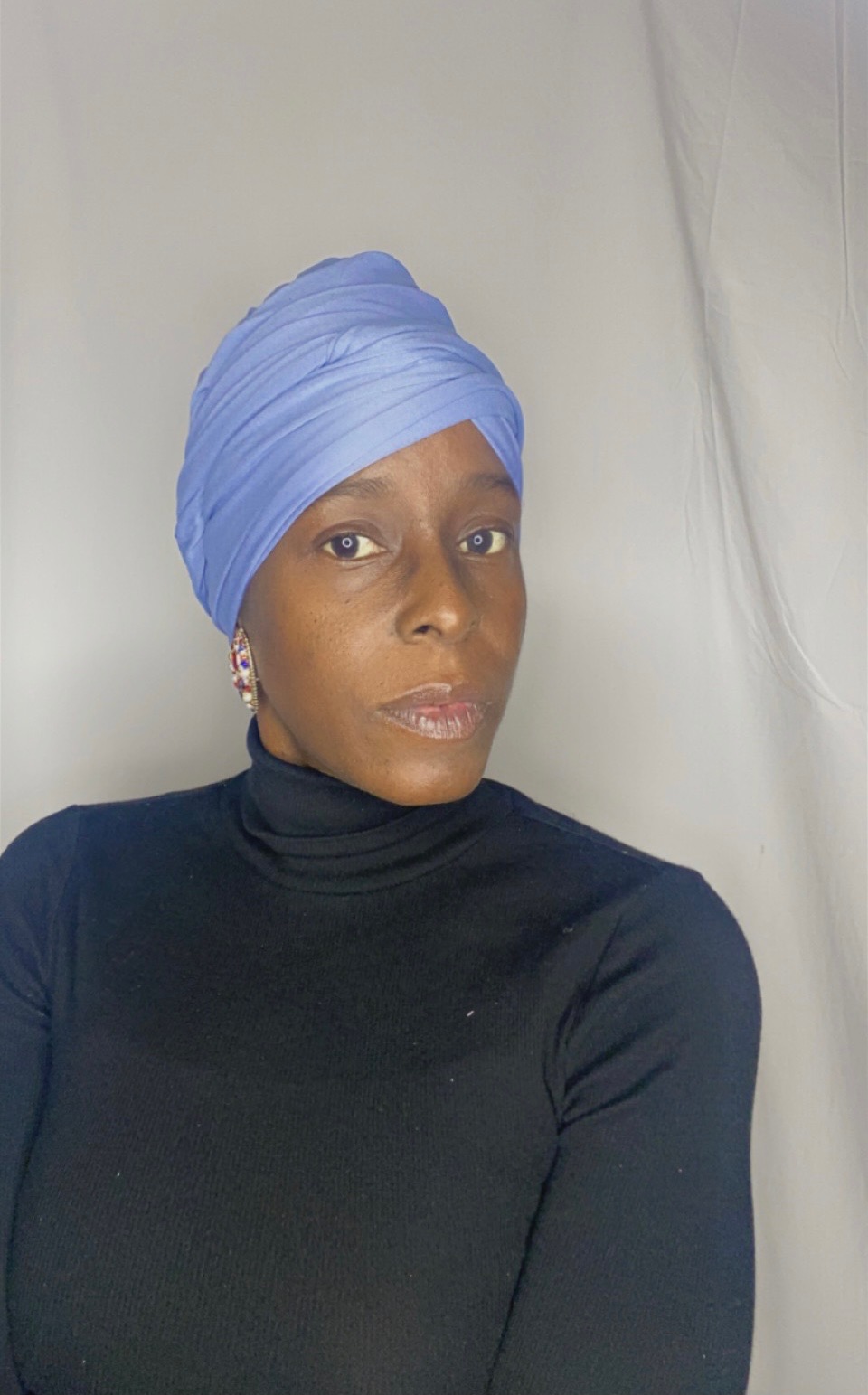 Portrait of a woman wearing a sky blue Krown wrapped as a full turban with a beaded statement earring